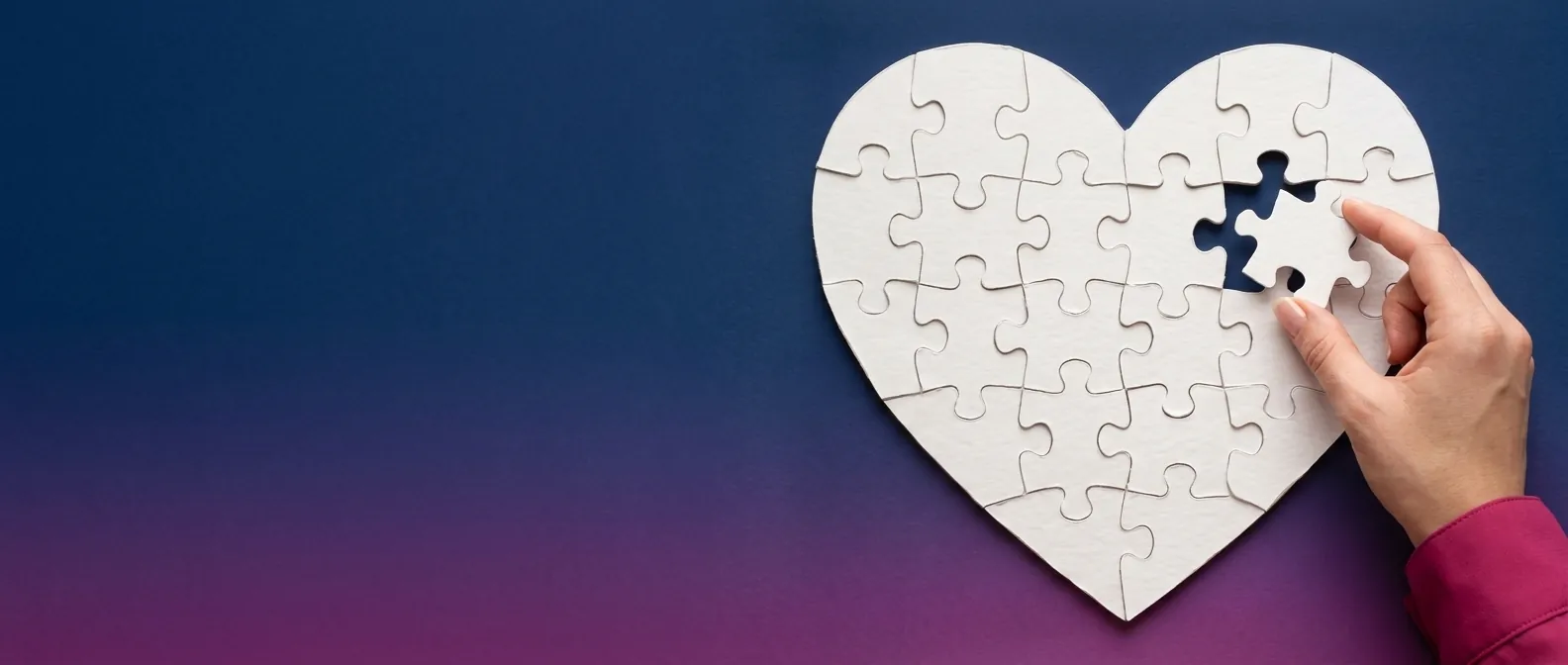 Magenta ruhaujjas kéz illeszti be a hiányzó darabot egy fehér puzzle-szívbe